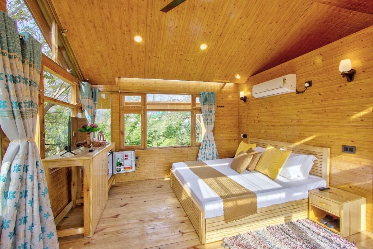 A wooden cabin bedroom with a bed, bedside table, and a desk with a chair.