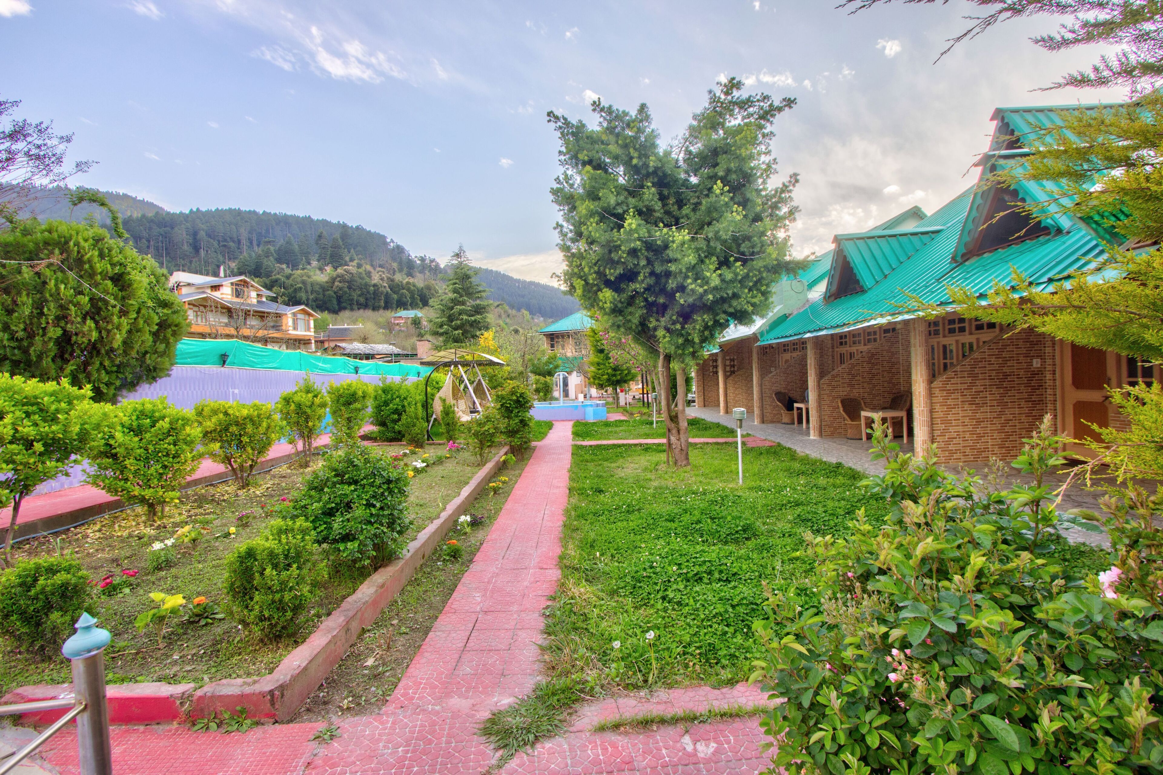 A pathway leading to a building with a green roof, surrounded by greenery and a mountainous backdrop.