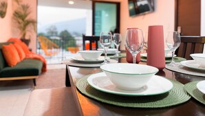 Un comedor con una mesa dispuesta para cuatro personas, que incluye cuencos, vasos y un florero rosa.