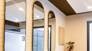 Un área de bar moderna con tres espejos grandes en la pared, una barra alargada y sillas blancas.