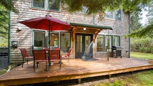 Eine Holzterrasse mit Gartenmöbeln und Grill, mit Blick auf ein bewaldetes Gebiet.