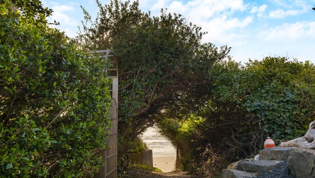 Ein Weg führt durch einen hölzernen Bogen hindurch zum Strand, umgeben von dichtem Grün.