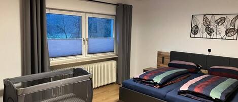 A bedroom with a bed, a radiator, a window with curtains, and a radiator below the window.