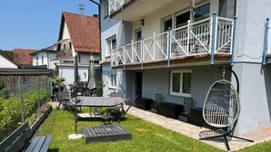 En boligbygning med balkon, terrasse med havemøbler og en hængestol.