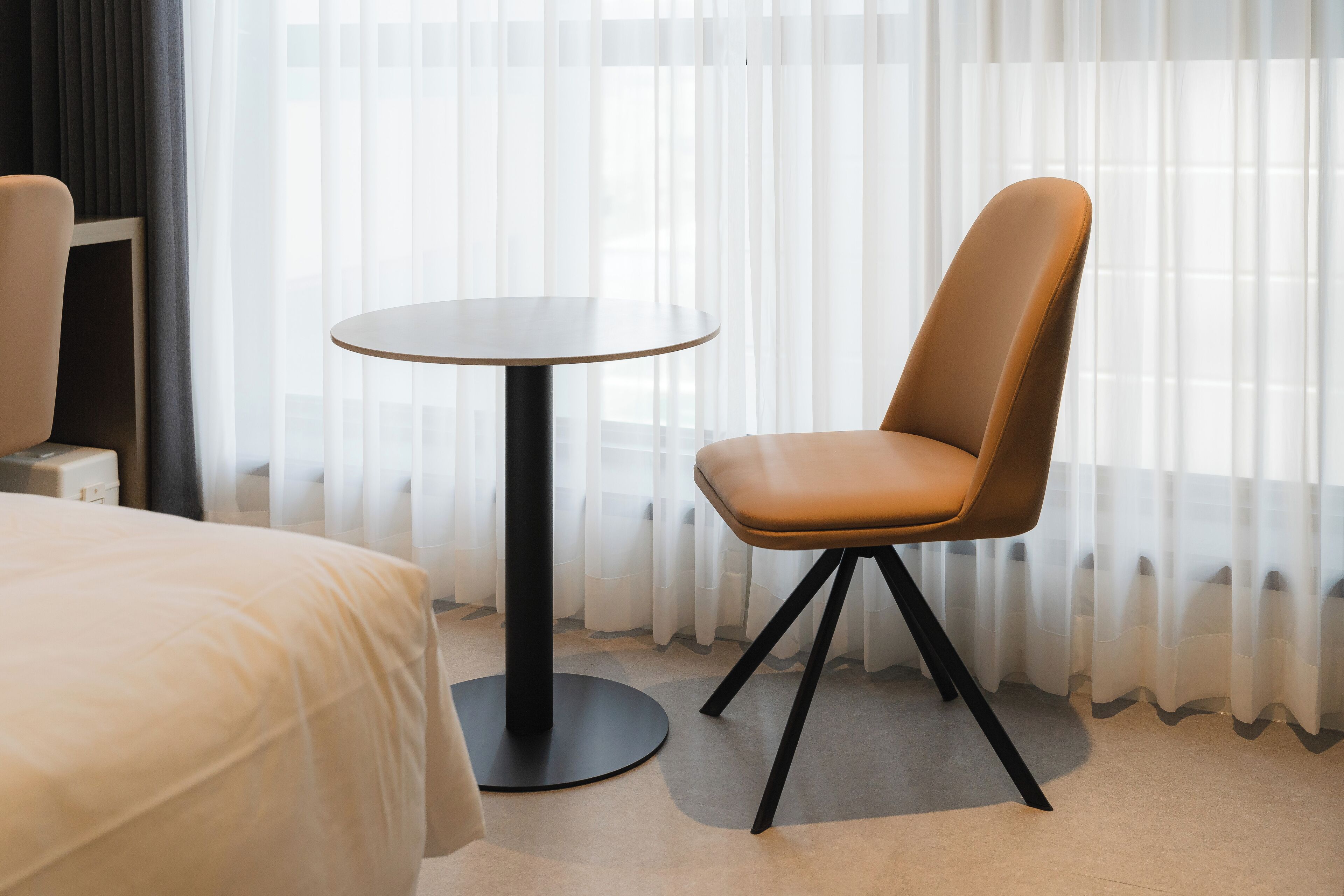A hotel room with a bed, a round table, and a chair.
