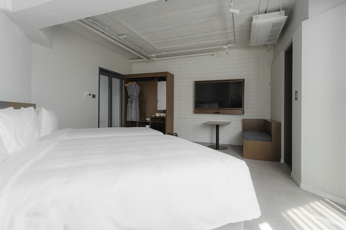 A modern hotel room with a large bed, a TV, a small desk, and a seating area.