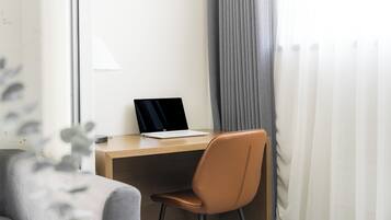 A modern office space with a laptop on a wooden desk, a brown chair, and a grey sofa.