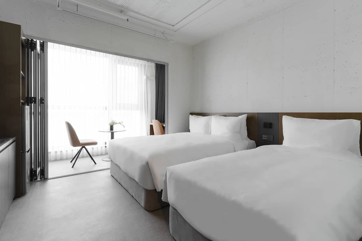 A hotel room with two beds, a small table, and a chair.