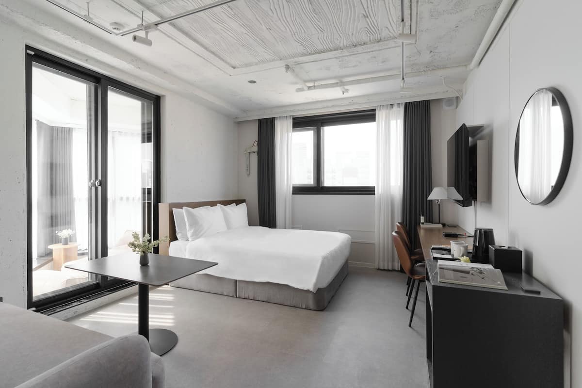 A modern hotel room with a large bed, a desk, a chair, a TV, and a window with curtains.