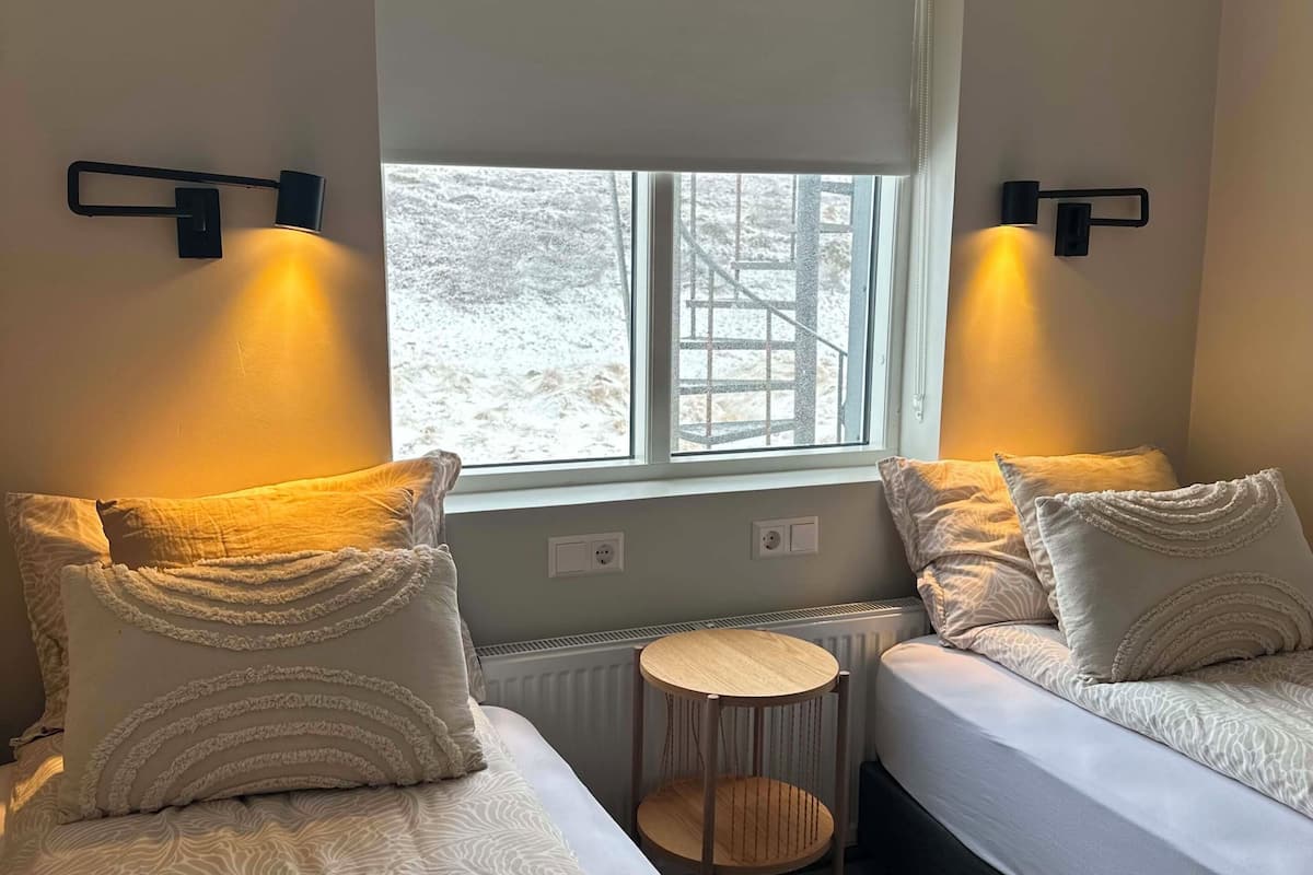 A room with two beds, a small round table, and a window with a view of a snowy landscape.