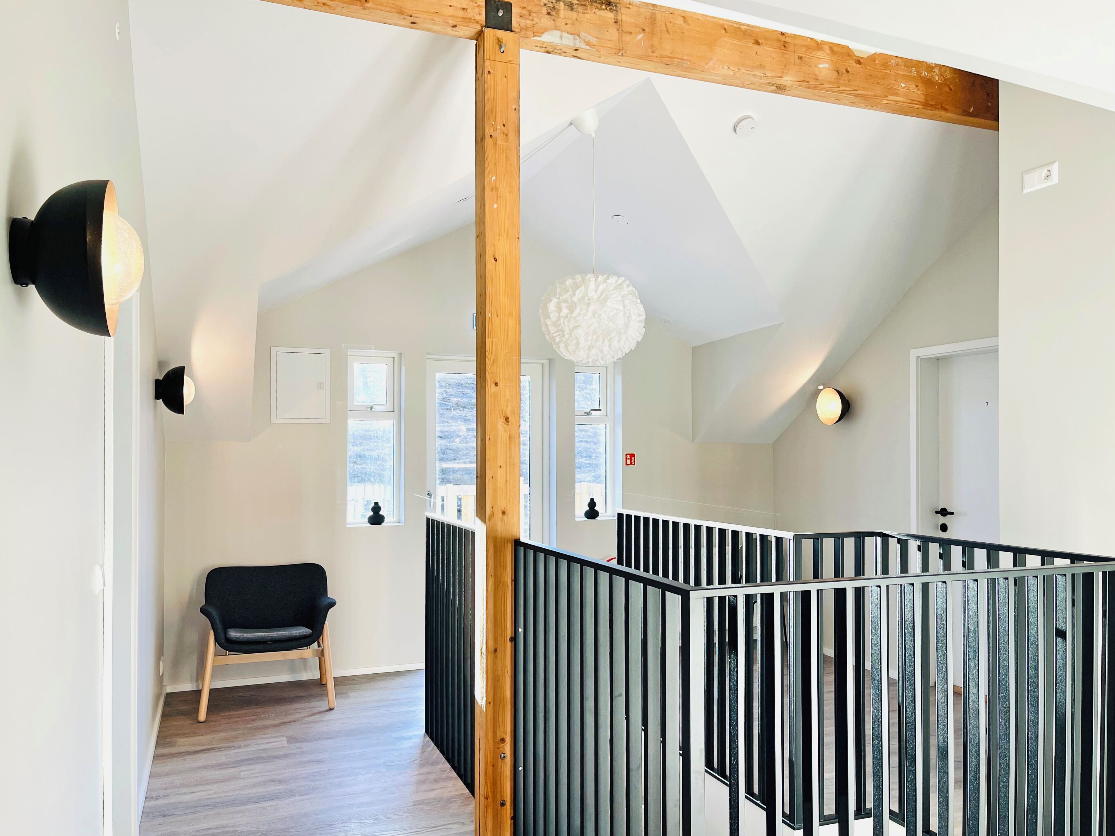 A modern interior with a wooden ceiling beam, a black chair, a white wall, and a black railing.