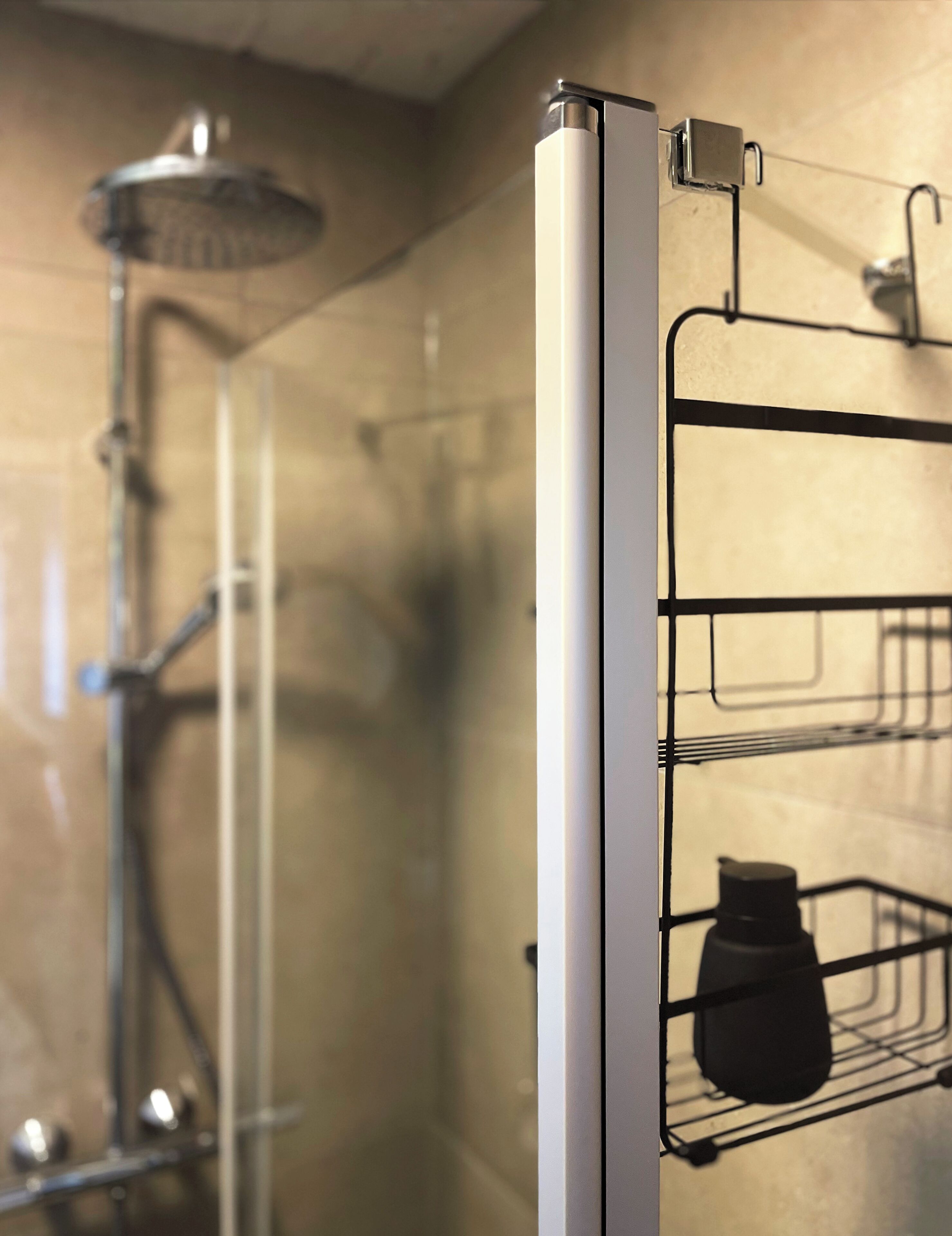 Une salle de bain avec une douche, un porte-serviettes et une étagère sur laquelle se trouve une bouteille.