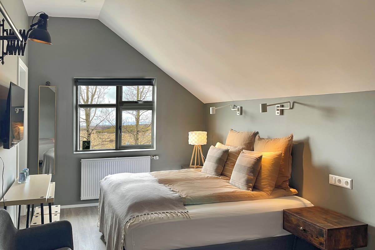A bedroom with a bed, bedside table, lamp, and a window with a view of trees.