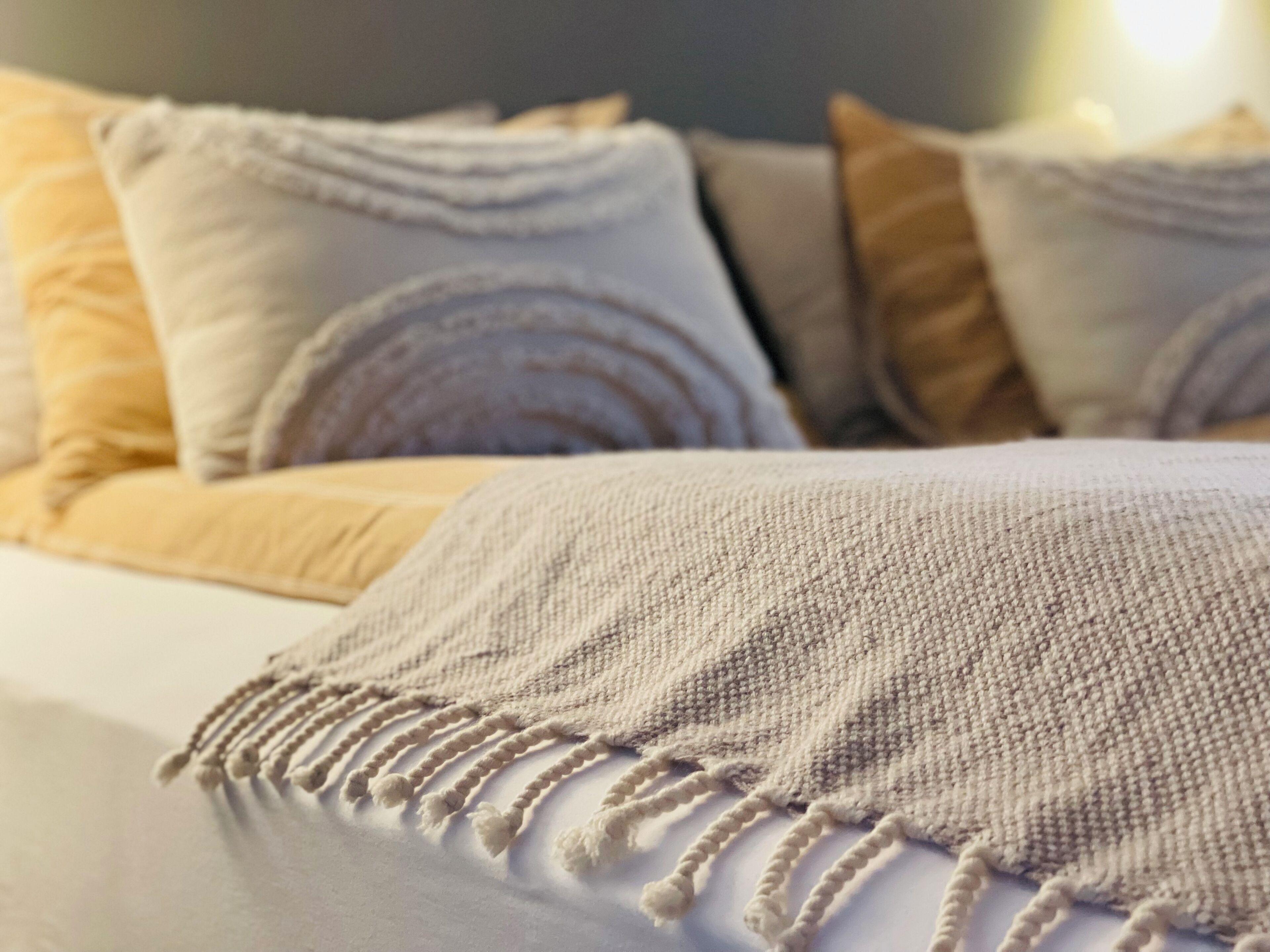 A bed with a textured blanket and multiple pillows in shades of beige and gray.