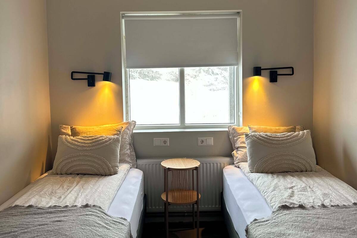 A room with two beds, a small table, a radiator, and a window with a view.