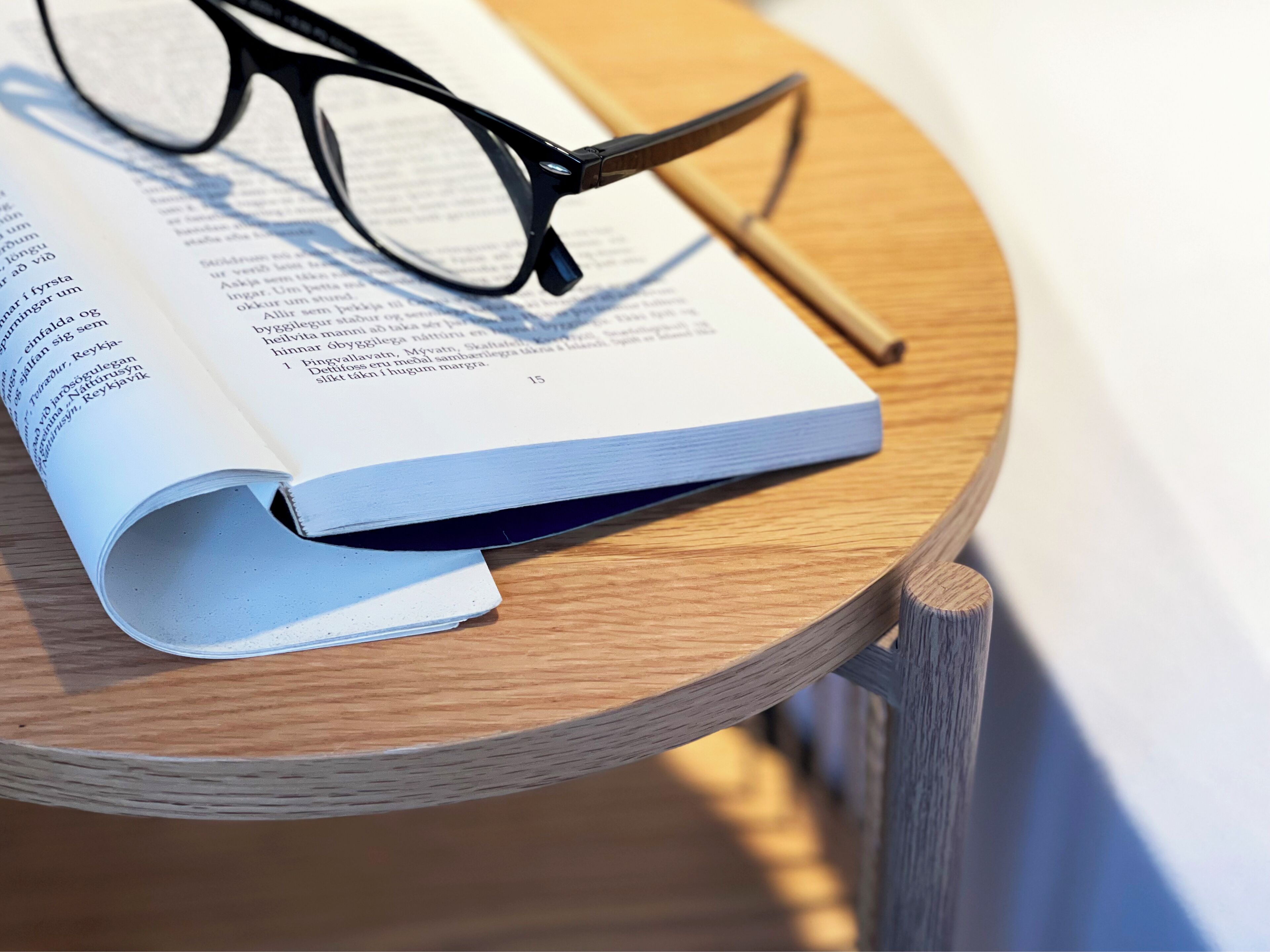A book open on a wooden table with a pair of glasses beside it.