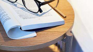 A book open on a wooden table with a pair of glasses beside it.
