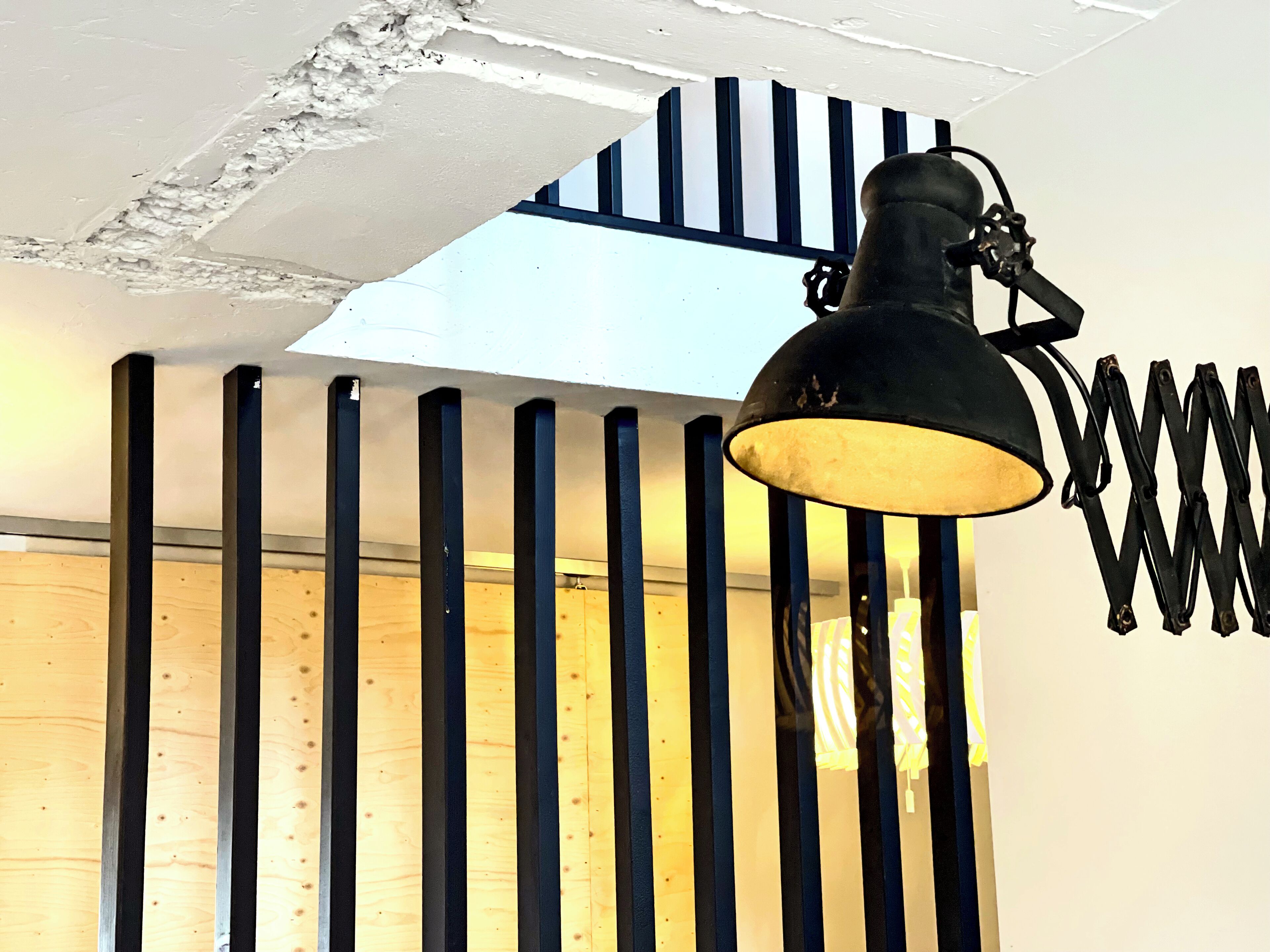 Una habitación con techo inclinado, lámpara colgante negra y vigas de madera.