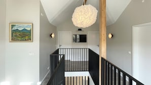 A modern staircase with black railings, a wooden beam ceiling, and a hanging light fixture. - Lindarholl Guesthouse (Egilsstaðir)