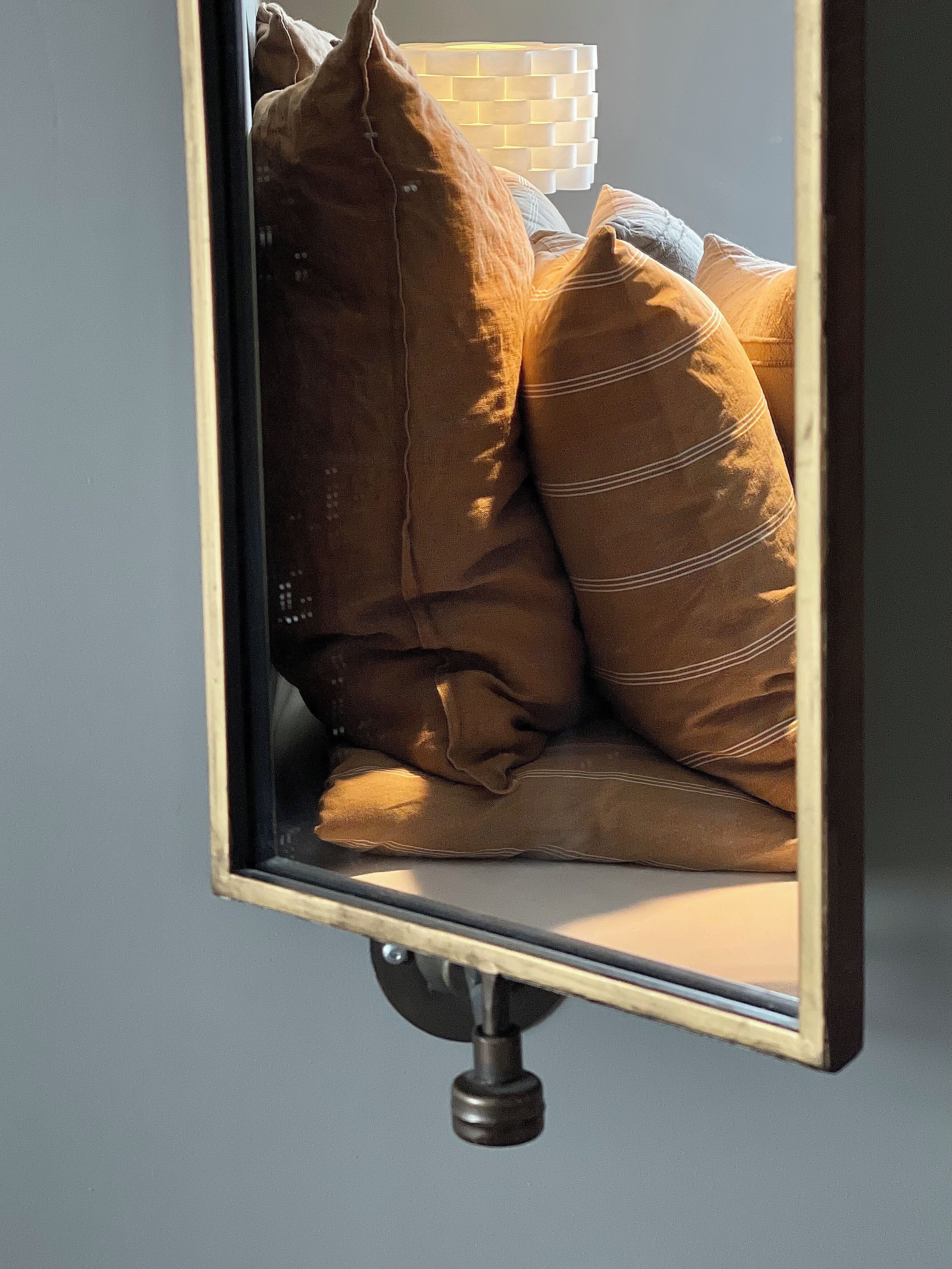 A mirror with a wooden frame reflecting a bed with multiple pillows.