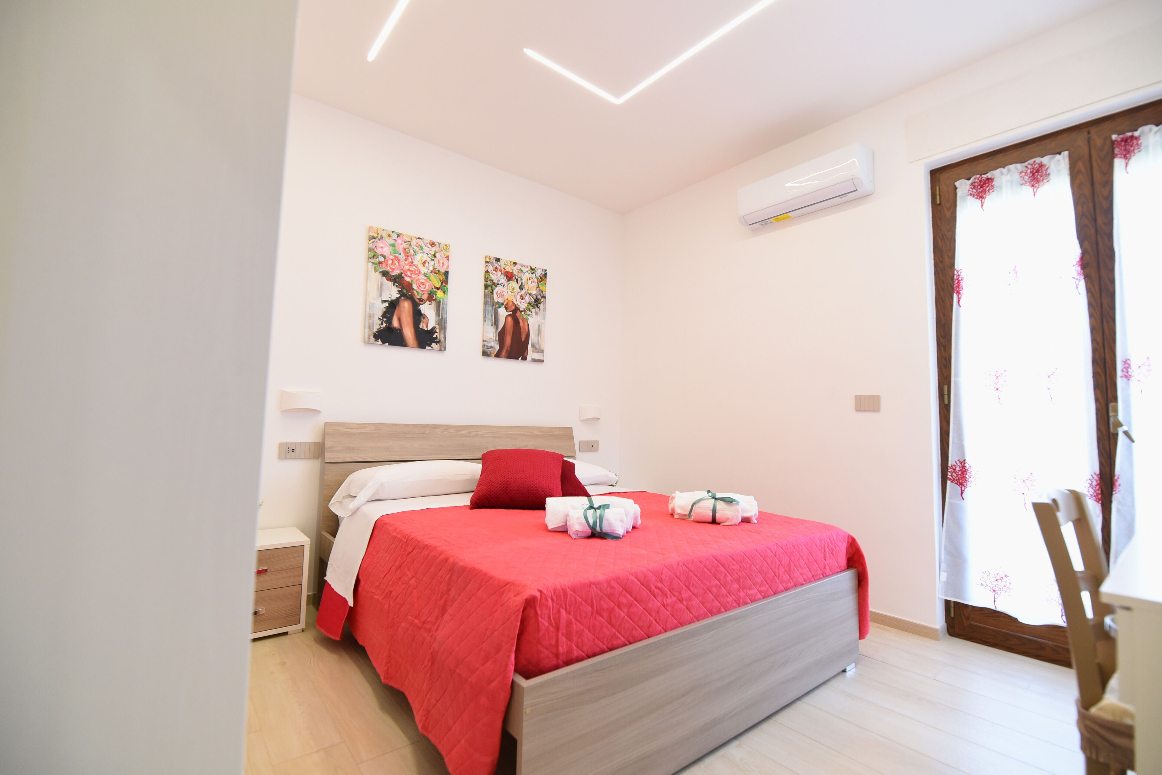 A bedroom with a bed, a nightstand, a chair, and two wall-mounted paintings.