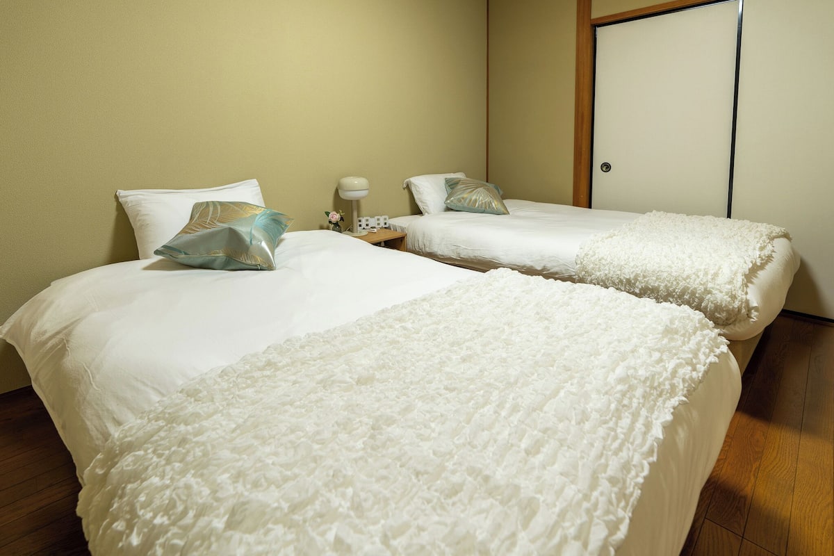 Two single beds with white linens and decorative pillows, a bedside table with a lamp, and a wooden floor.
