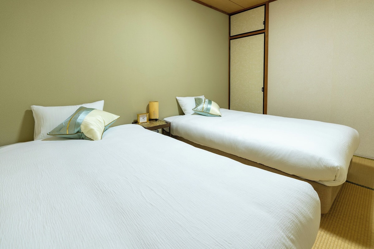 A hotel room with two single beds, a small bedside table with a lamp, and a traditional sliding door.