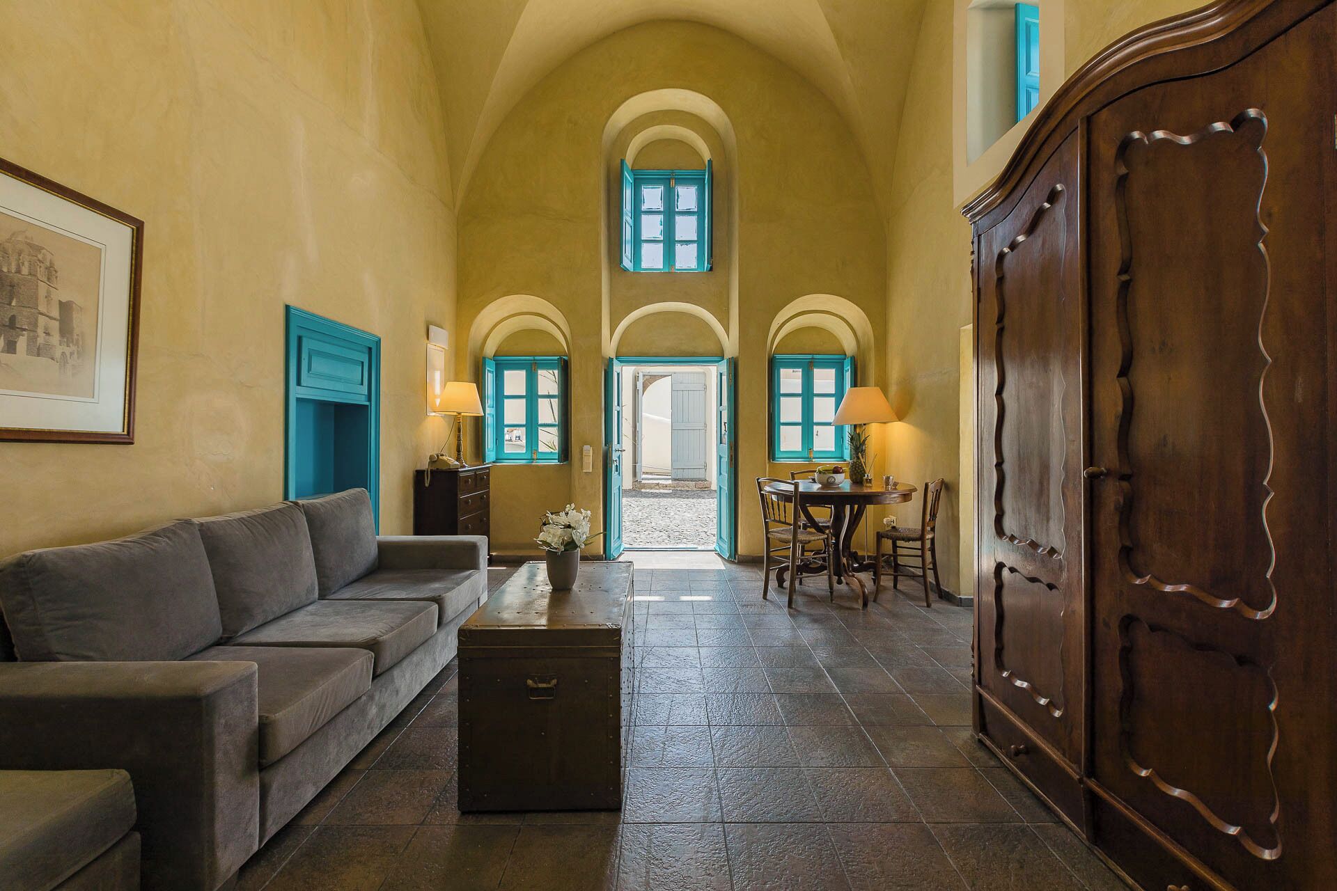 A room with a sofa, a table with chairs, a cabinet, and a view through an arched doorway.