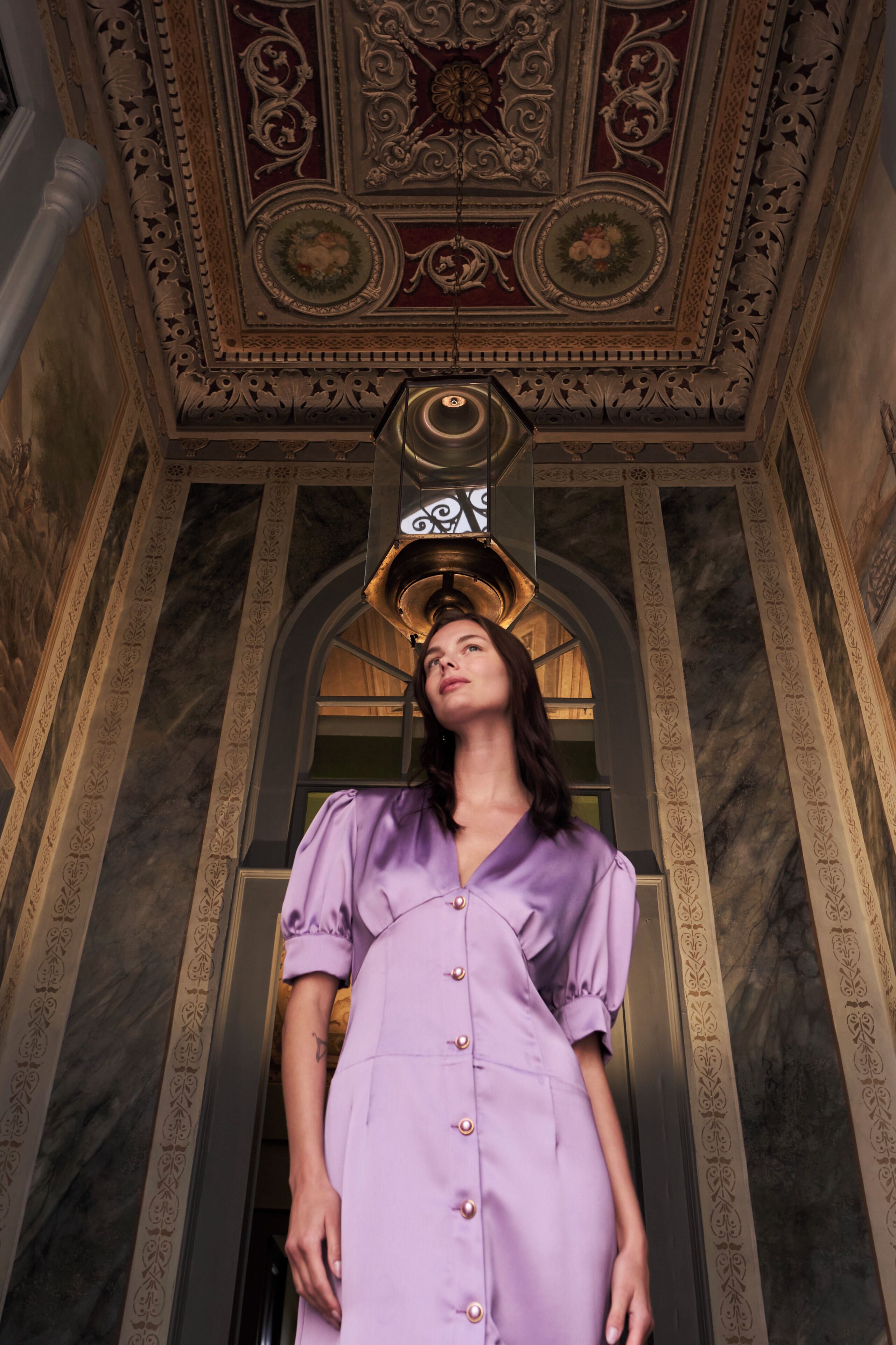A person standing in a room with ornate ceiling and marble walls.