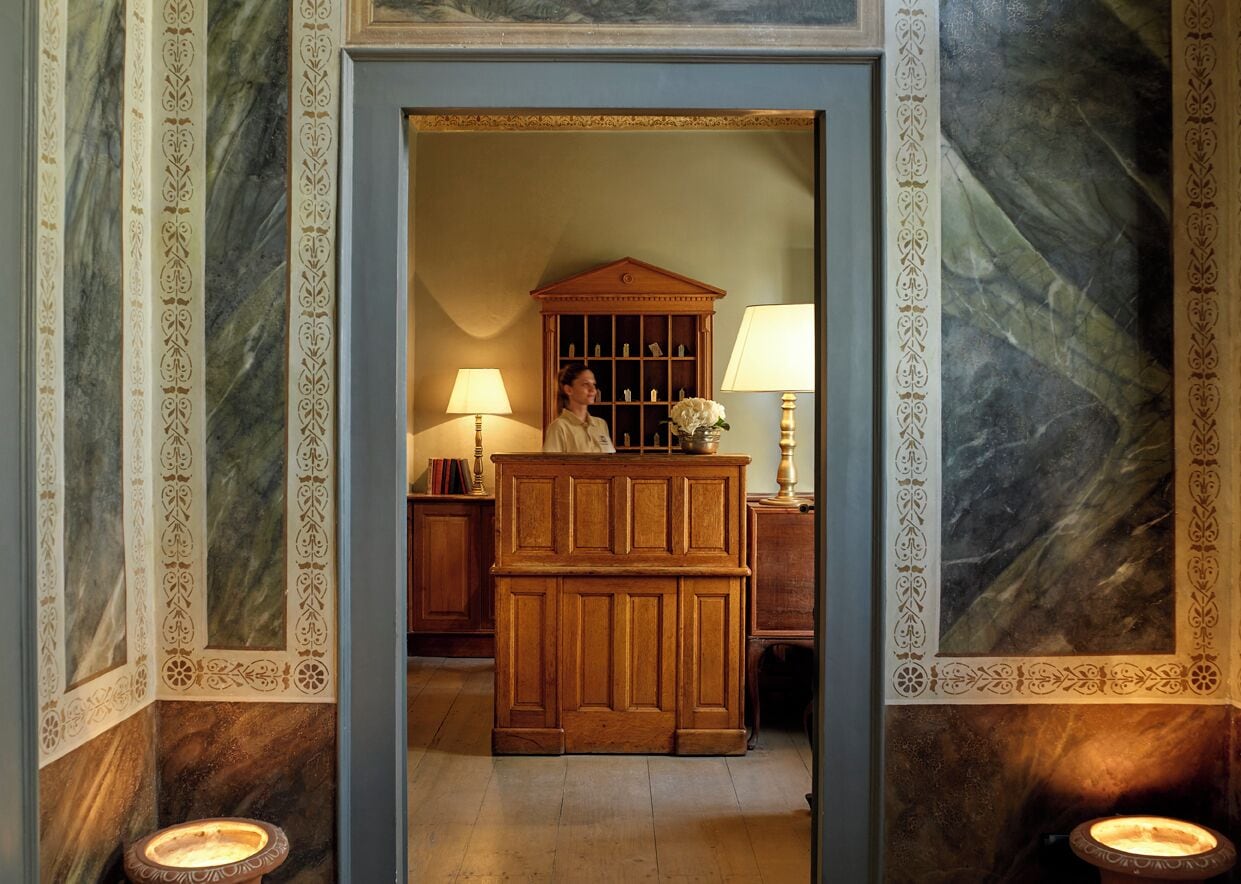 A hallway with a wooden desk, two lamps, and a decorative cabinet.