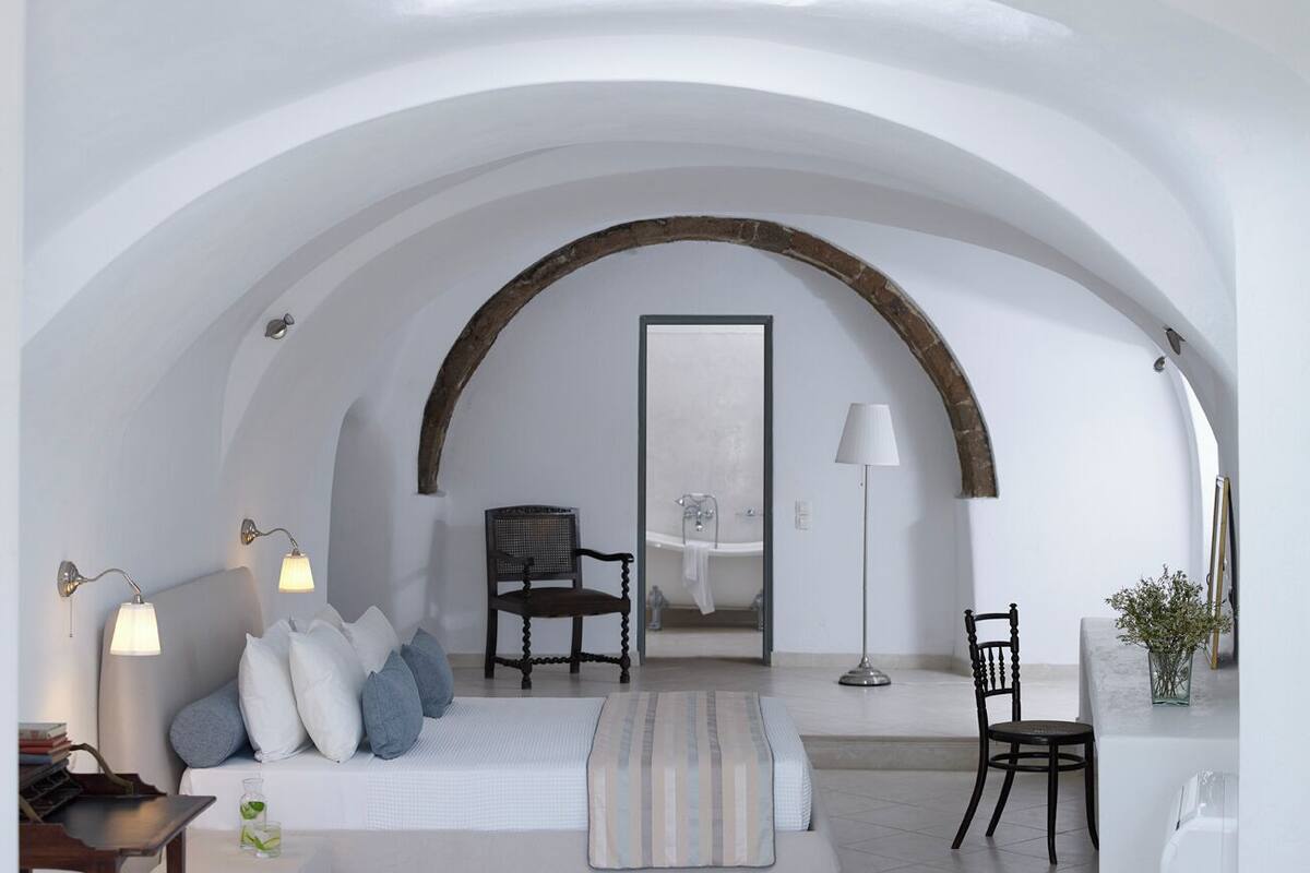 A modern interior with a high arched ceiling, a sofa with cushions, a chair, a lamp, and a view into a bathroom.