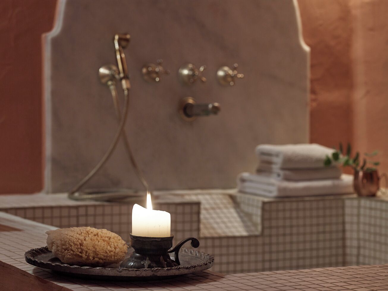 Une salle de bain avec une baignoire, une pile d’serviettes et une bougie allumée posée sur un plateau.