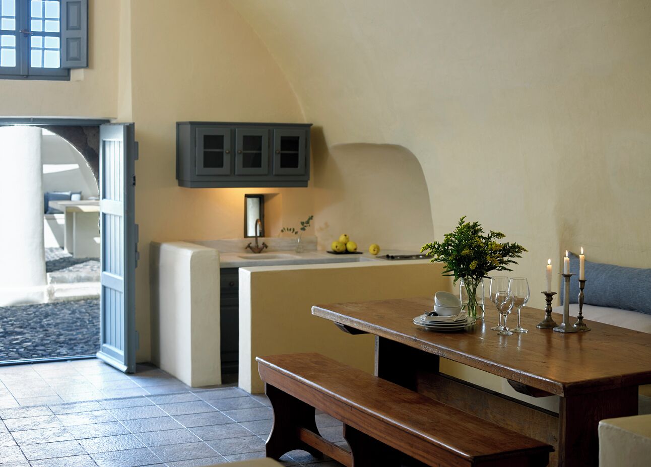 A dining area with a wooden table, benches, a kitchen area with a counter, and a grey cabinet.