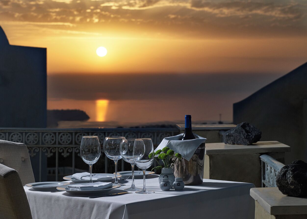 A table set for dining with wine glasses and a bottle, overlooking a sunset over water.