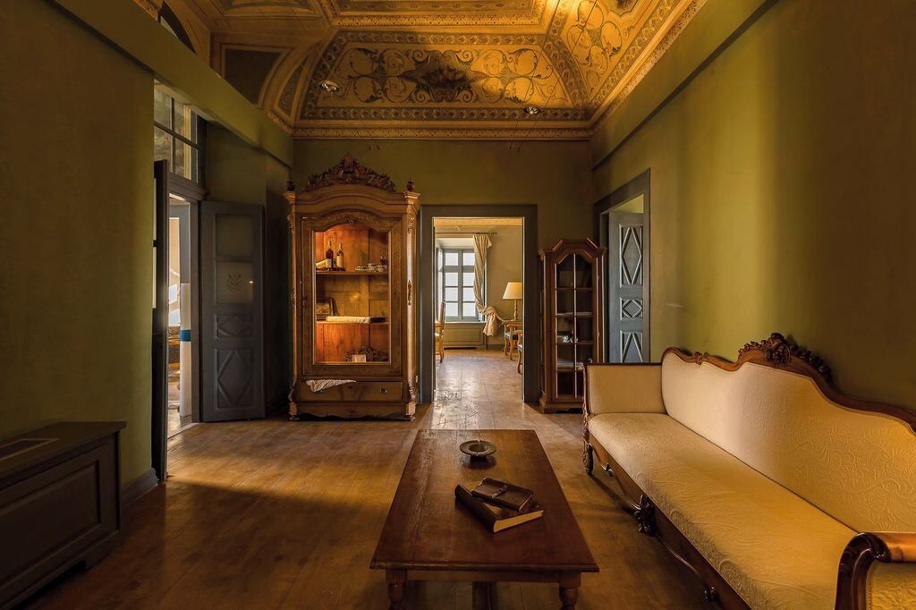 A room with a wooden floor, a sofa, a table with books, and a cabinet with glass doors.