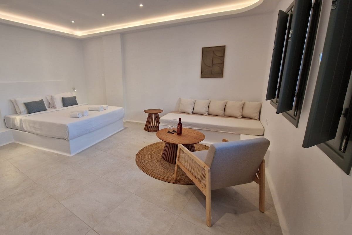 A modern hotel room with a bed, sofa, round wooden table, and a chair.