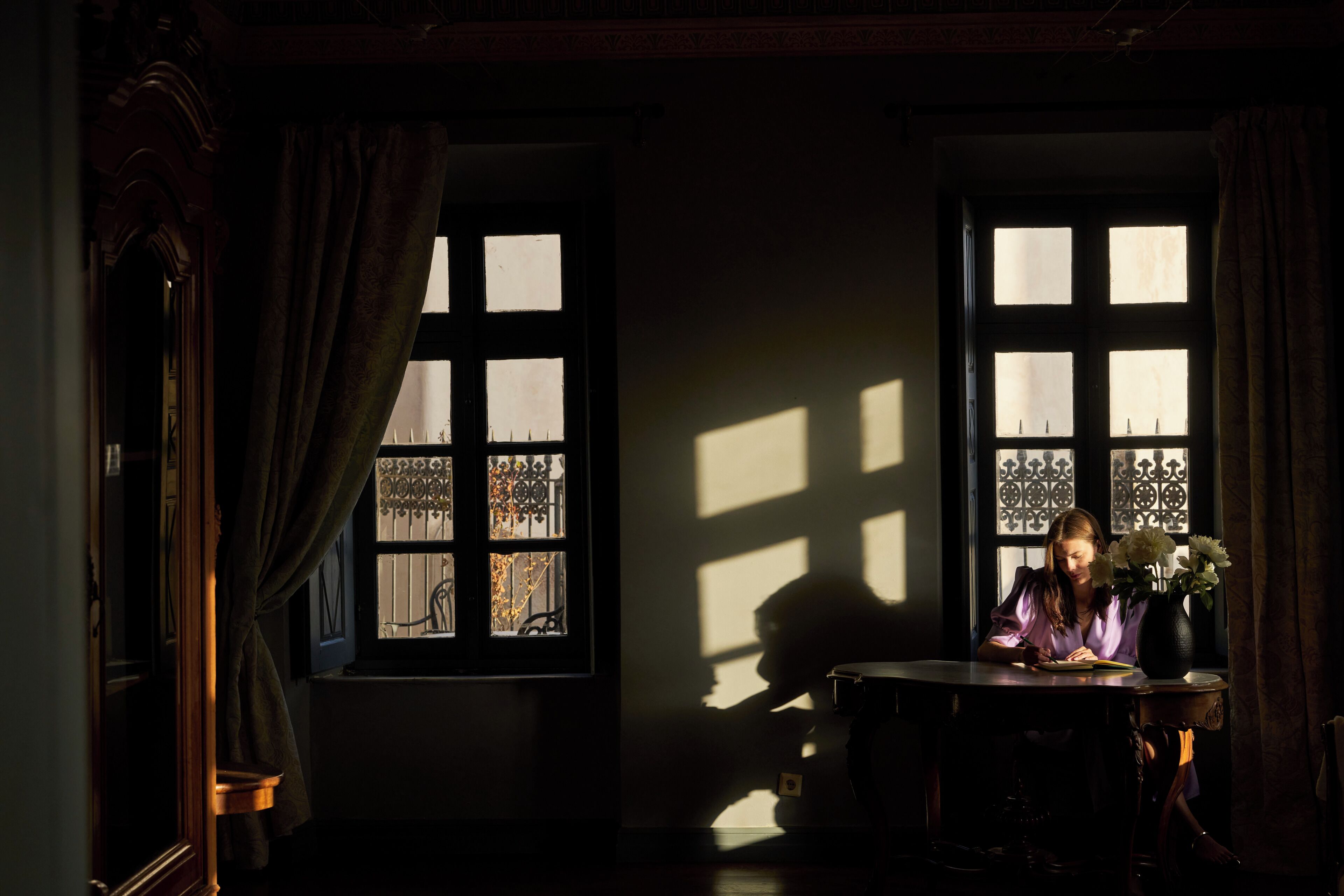 A room with a large window, a table with a vase of flowers, and a chair.