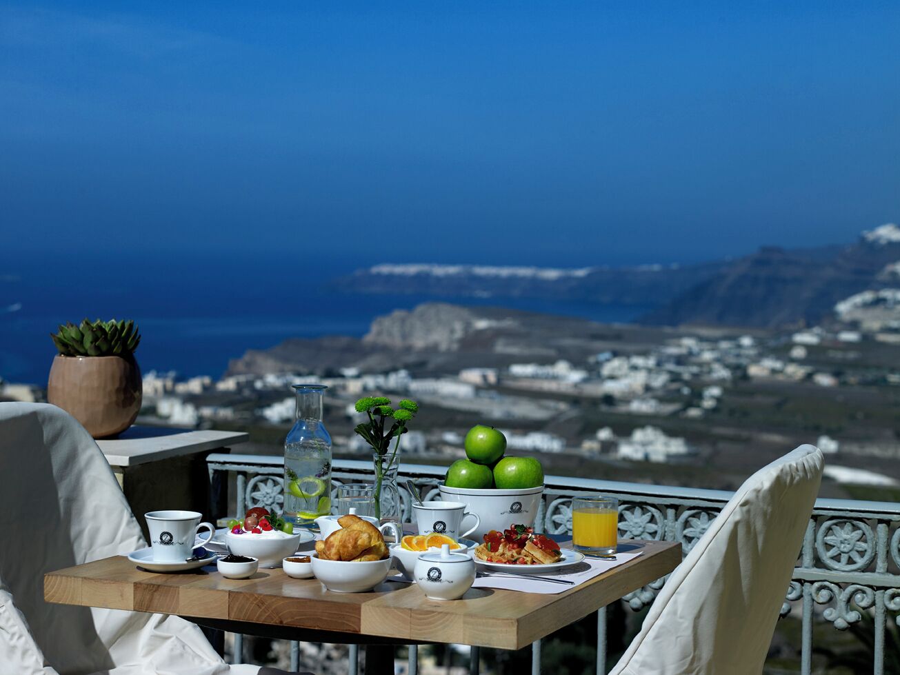 A table with breakfast items, a potted plant, and a view of a coastal landscape.