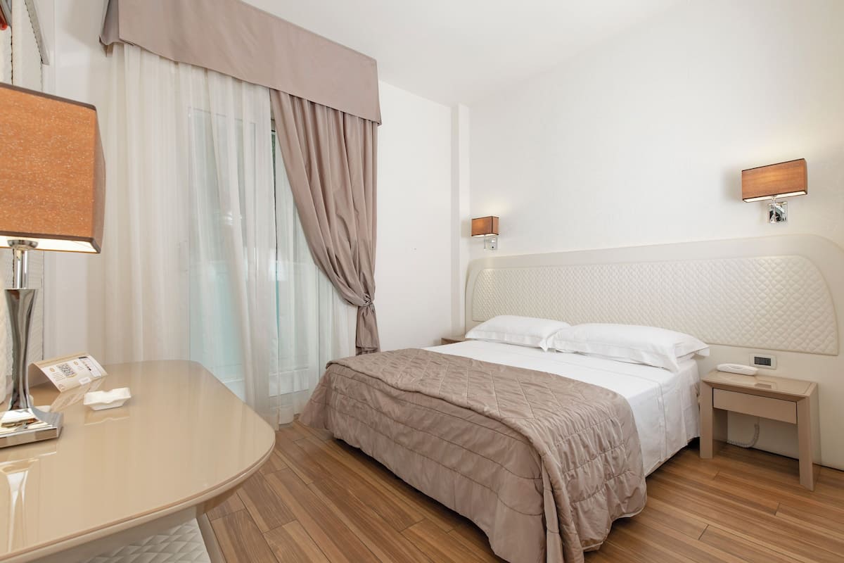 A hotel room with a bed, bedside table, lamp, and curtains.