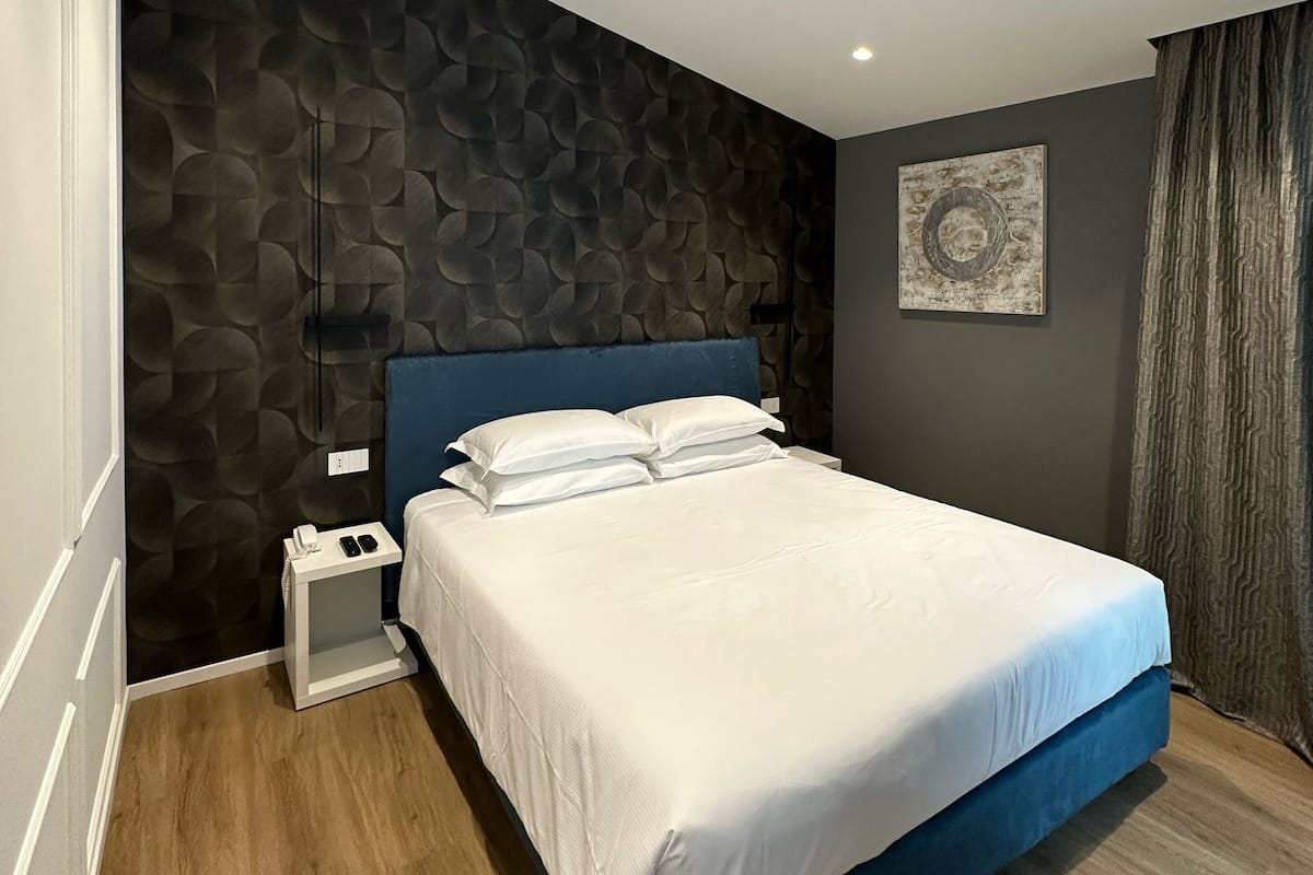 A modern bedroom with a large bed, a nightstand, a wall-mounted artwork, and a textured wall.