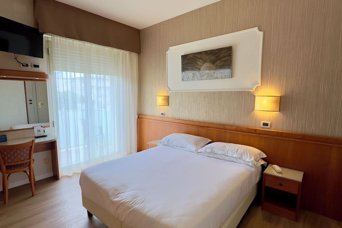 A hotel room with a large bed, a desk, a chair, a TV, and a painting on the wall.