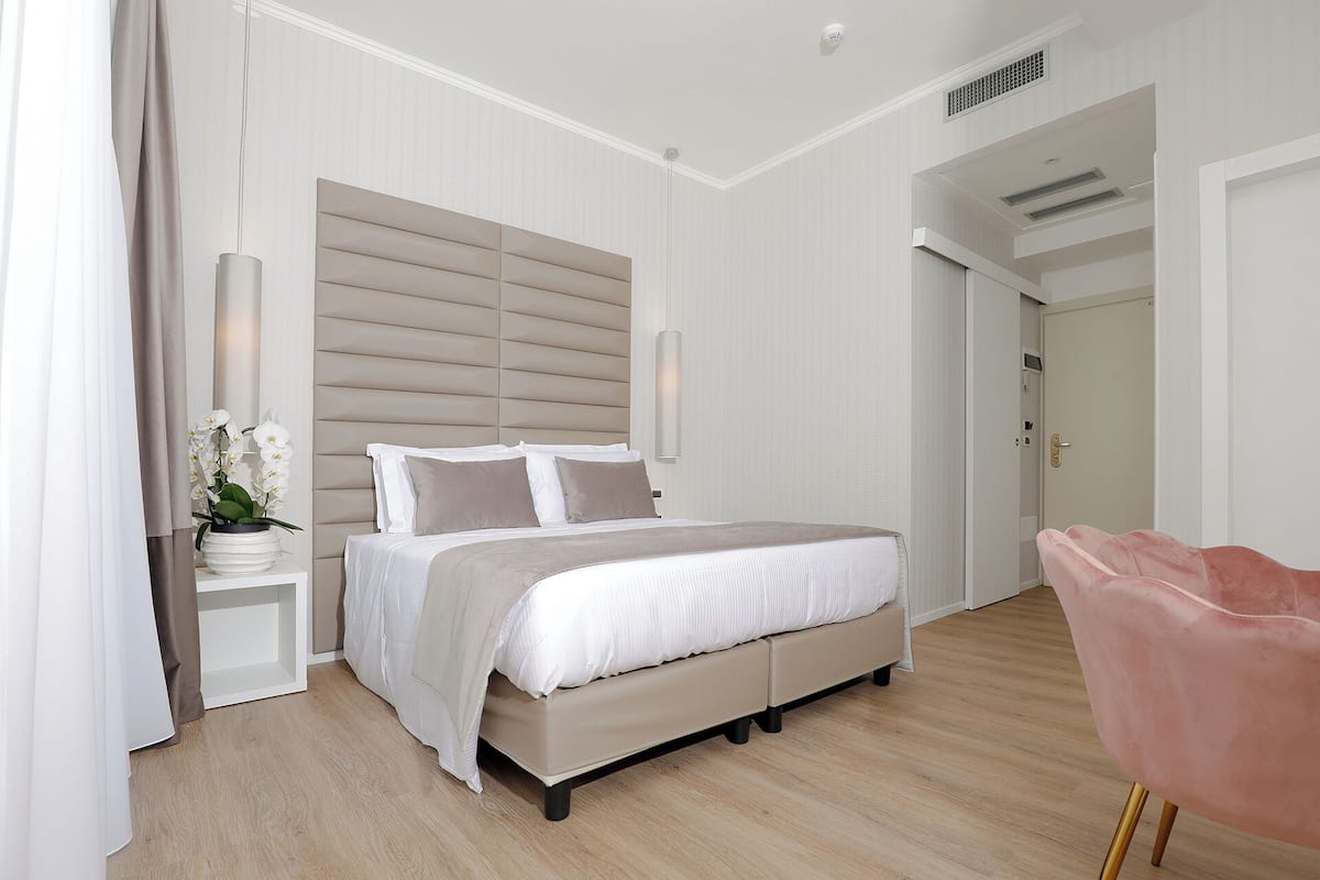 A bedroom with a bed, bedside tables, a nightstand, a pink chair, and a potted plant.