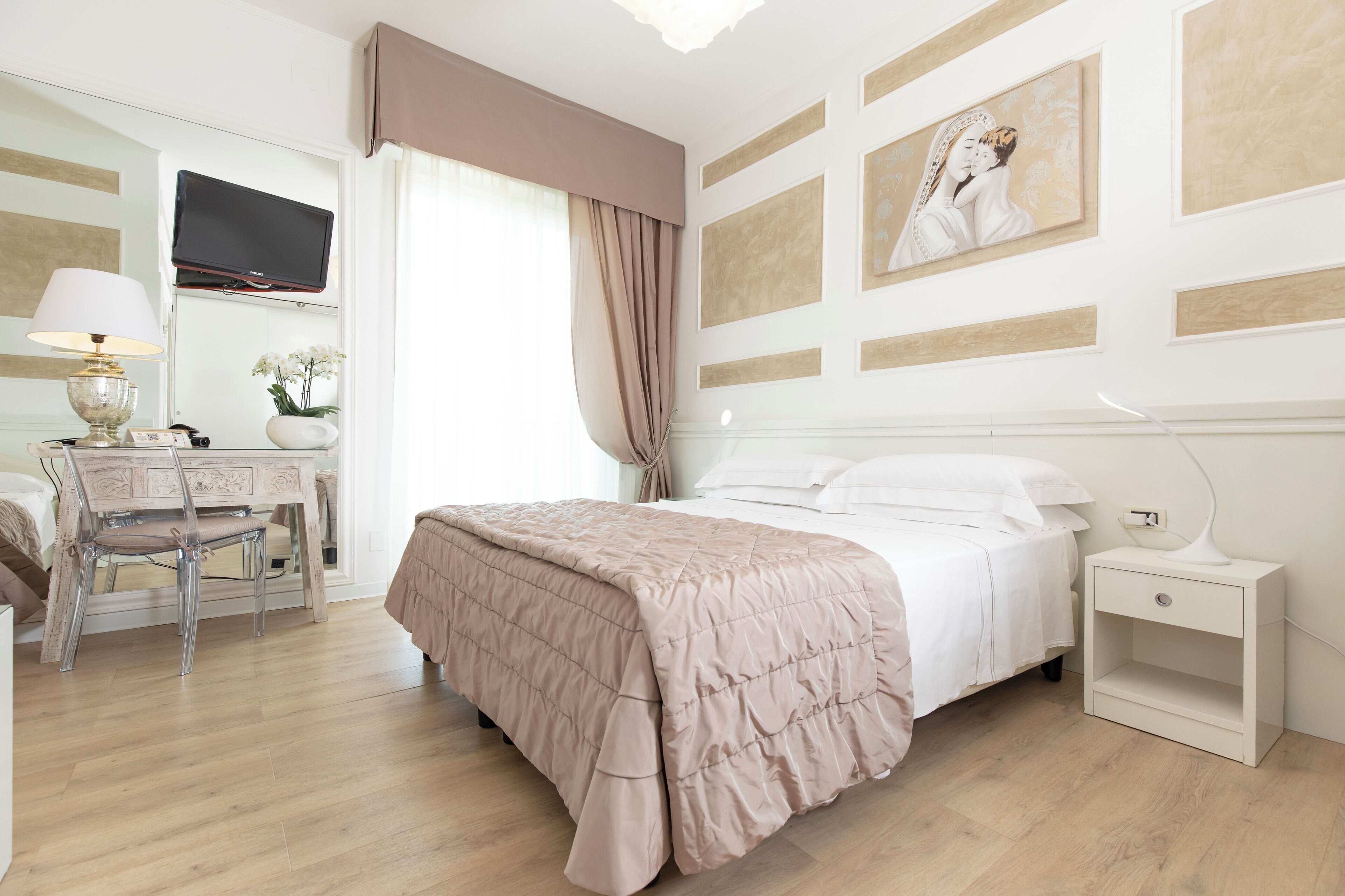 Ein Hotelzimmer mit Bett, Nachttisch, Lampe, Schreibtisch, Stuhl und einem an der Wand befestigten Fernseher.