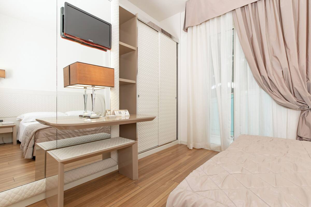 A modern hotel room with a bed, a desk with a lamp, a television, and a sliding door closet.