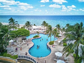 A resort pool with a view of the ocean, surrounded by palm trees and lounge chairs.