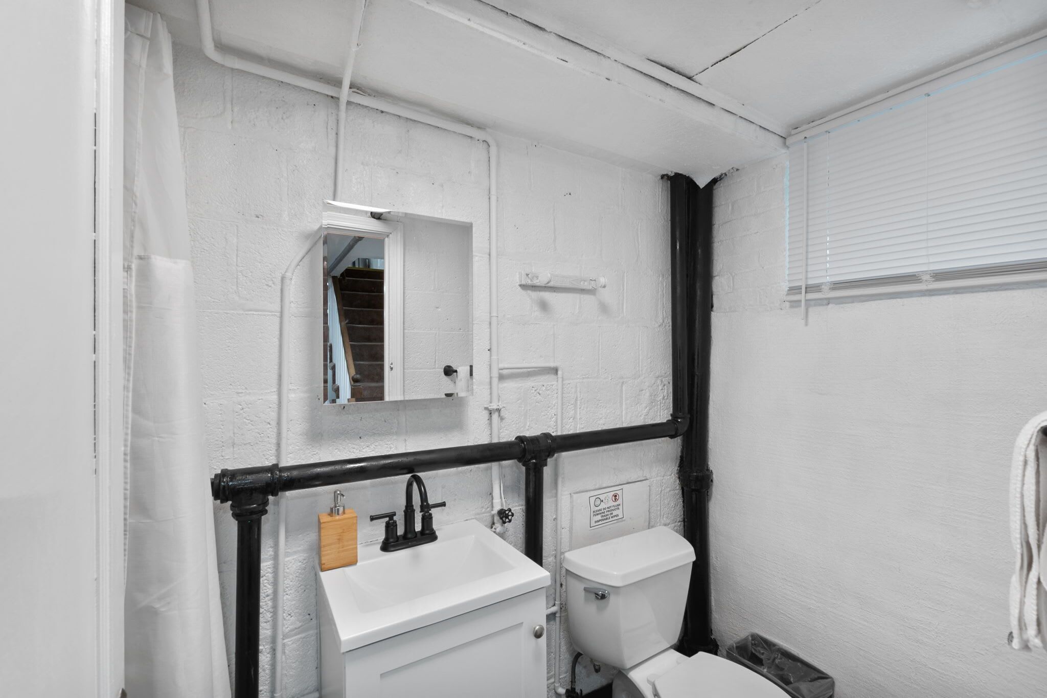 Une petite salle de bain aux murs blancs, avec un lavabo blanc, des toilettes et un miroir au-dessus du lavabo.