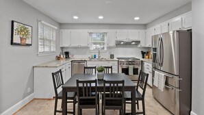 A modern kitchen with white cabinets, stainless steel appliances, and a dining area with a table and chairs.