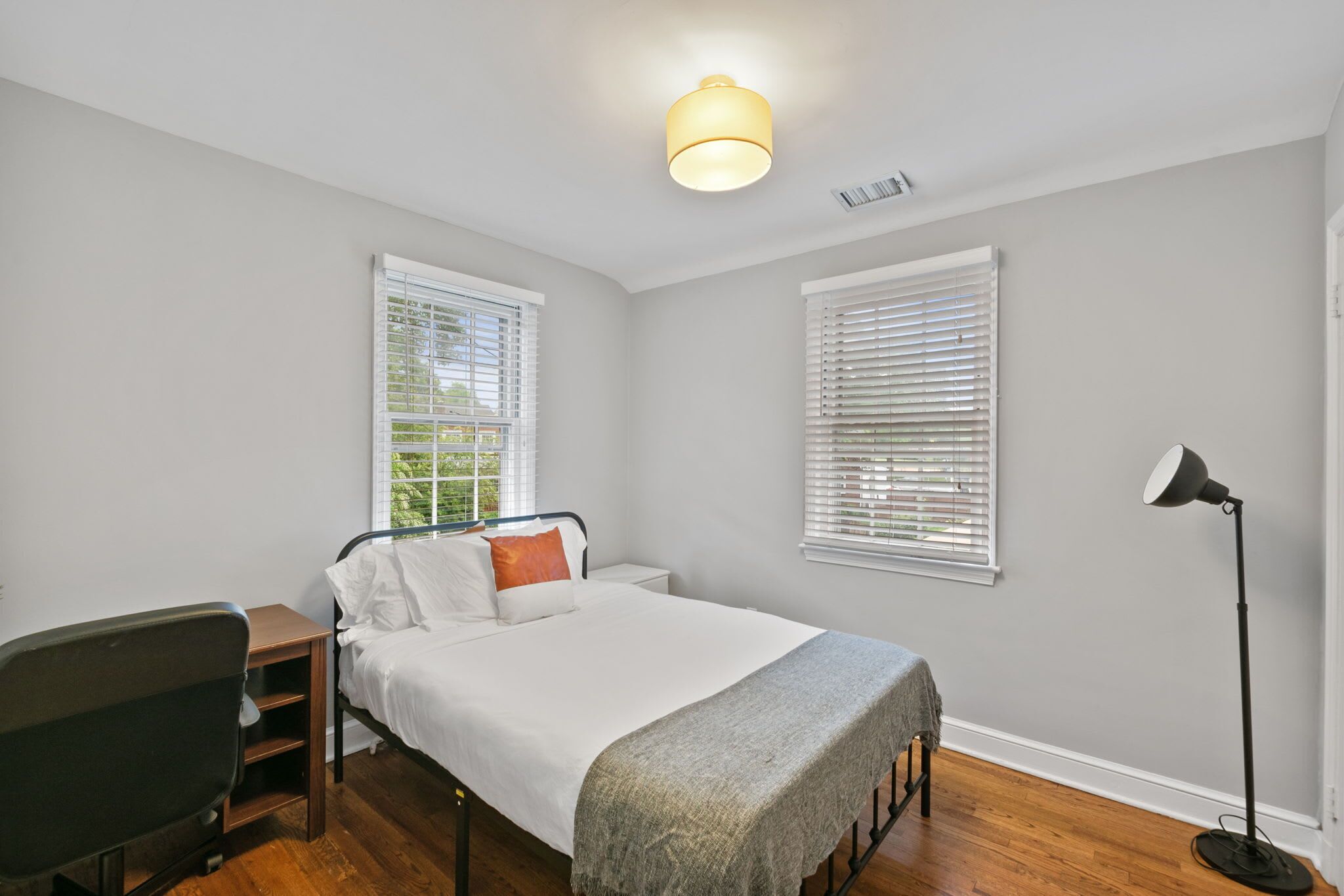 A bedroom with a bed, a desk, a chair, and a floor lamp.