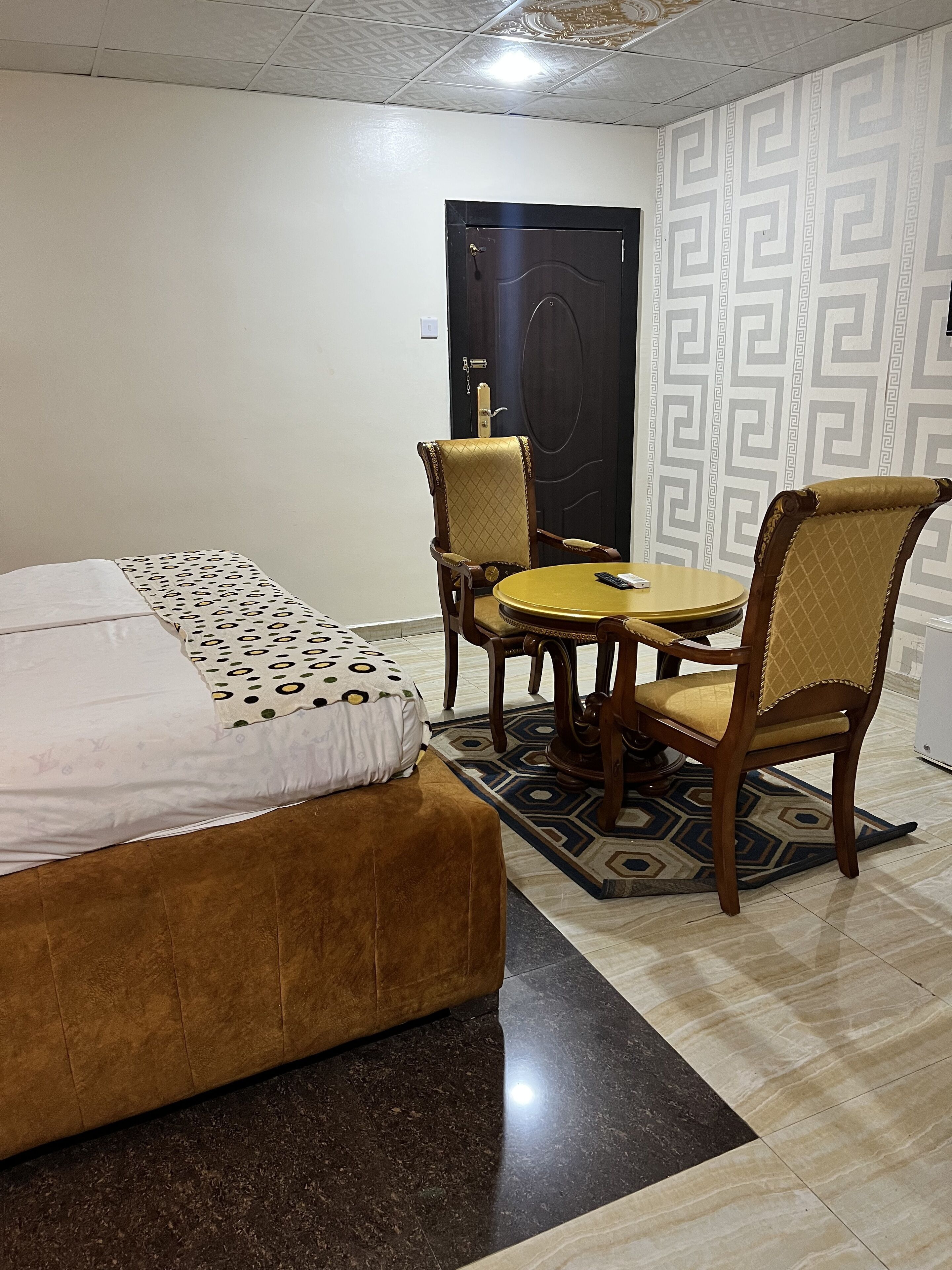 Habitación de hotel con cama, dos sillas, una mesita y un tapete estampado.