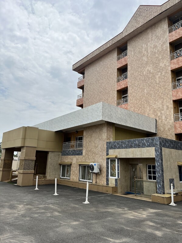 Un hotel de varios pisos con fachada color beige y gris, balcones con barandillas metálicas y una unidad de aire acondicionado montada en la pared exterior.